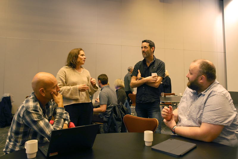 To personer står  og to sitter ved bordet ved sinden av