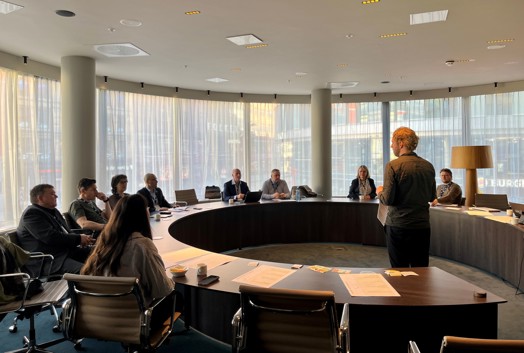 Vi ser et stort ovalt bord i møterommet hvor det sitter folk rundt, og Eirik Haglund står i midten.