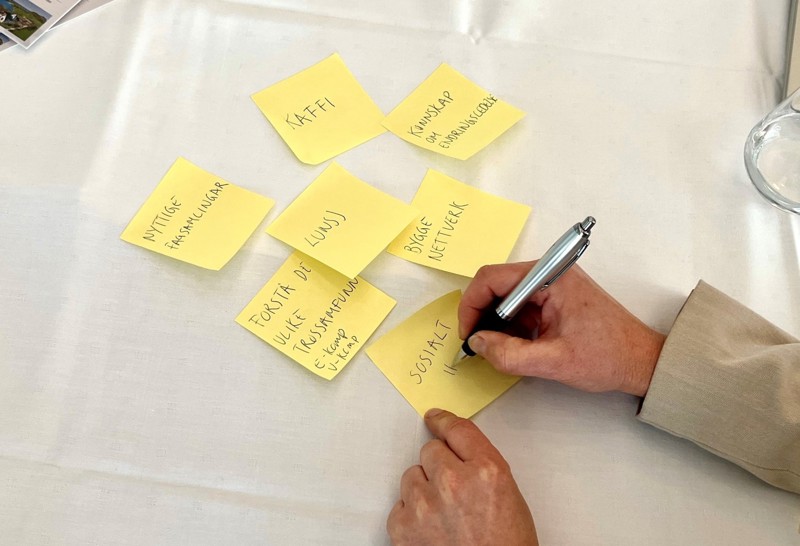 Bildet viser to hender som skriver på en postit-lapp.